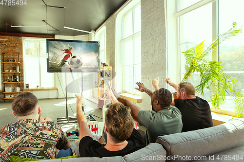 Image of Group of friends watching football or soccer game on TV at home