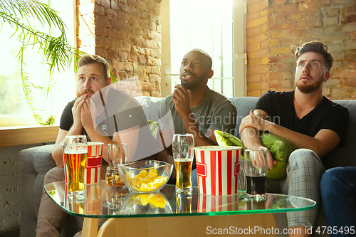 Image of Group of friends watching football or soccer game on TV at home