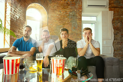 Image of Group of friends watching football or soccer game on TV at home