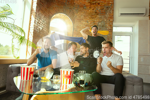 Image of Group of friends watching football or soccer game on TV at home