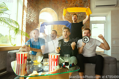 Image of Group of friends watching football or soccer game on TV at home