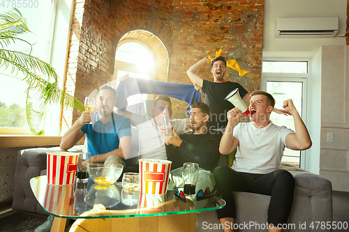 Image of Group of friends watching football or soccer game on TV at home