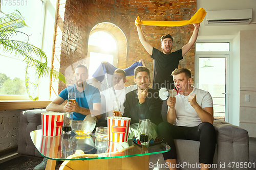 Image of Group of friends watching football or soccer game on TV at home