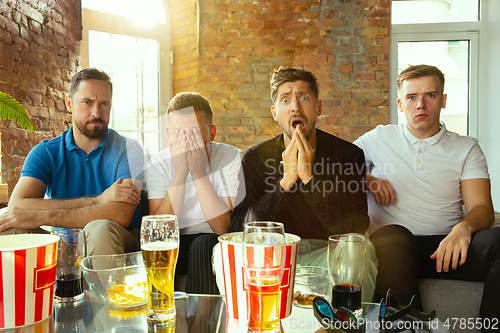 Image of Group of friends watching football or soccer game on TV at home