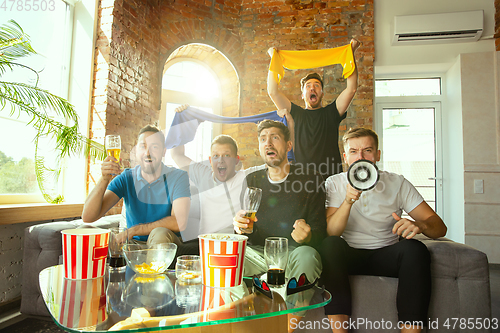 Image of Group of friends watching football or soccer game on TV at home