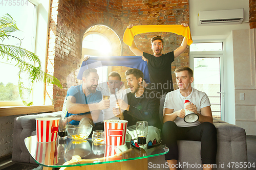 Image of Group of friends watching football or soccer game on TV at home