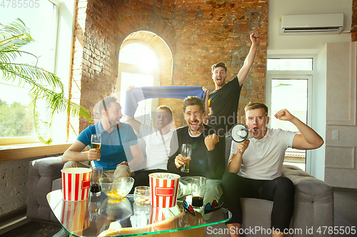 Image of Group of friends watching football or soccer game on TV at home