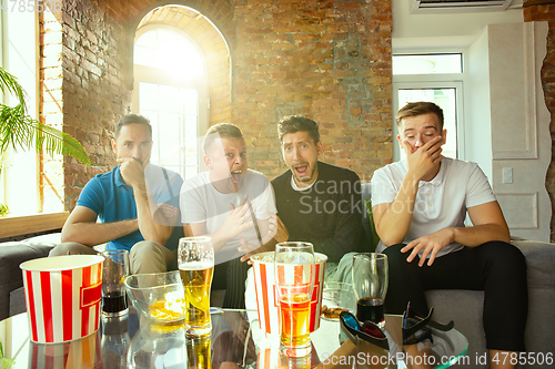 Image of Group of friends watching football or soccer game on TV at home