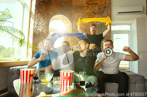 Image of Group of friends watching football or soccer game on TV at home