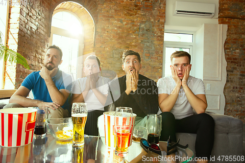 Image of Group of friends watching football or soccer game on TV at home