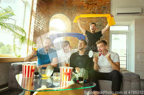 Image of Group of friends watching football or soccer game on TV at home