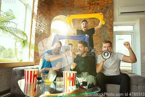 Image of Group of friends watching football or soccer game on TV at home