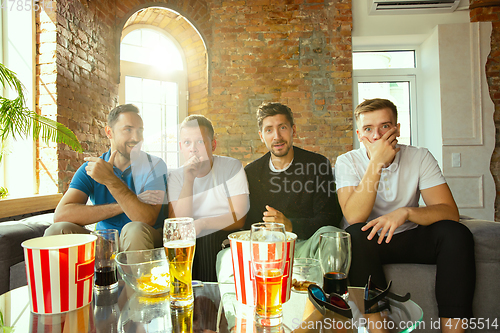 Image of Group of friends watching football or soccer game on TV at home