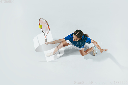 Image of Young woman in blue shirt playing tennis. Youth, flexibility, power and energy.