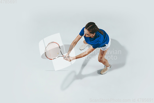 Image of Young woman in blue shirt playing tennis. Youth, flexibility, power and energy.