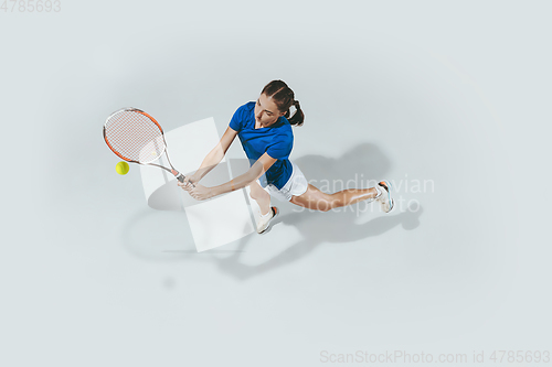 Image of Young woman in blue shirt playing tennis. Youth, flexibility, power and energy.