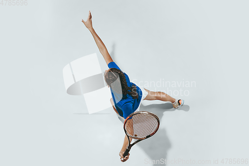 Image of Young woman in blue shirt playing tennis. Youth, flexibility, power and energy.