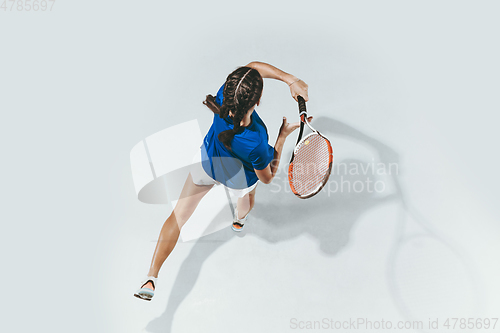 Image of Young woman in blue shirt playing tennis. Youth, flexibility, power and energy.