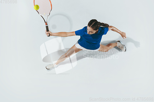 Image of Young woman in blue shirt playing tennis. Youth, flexibility, power and energy.