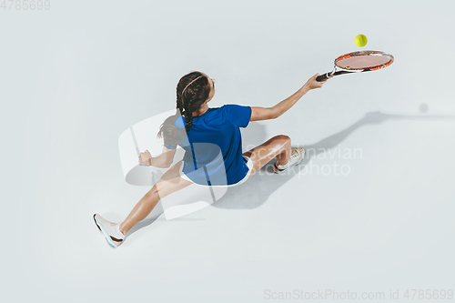 Image of Young woman in blue shirt playing tennis. Youth, flexibility, power and energy.