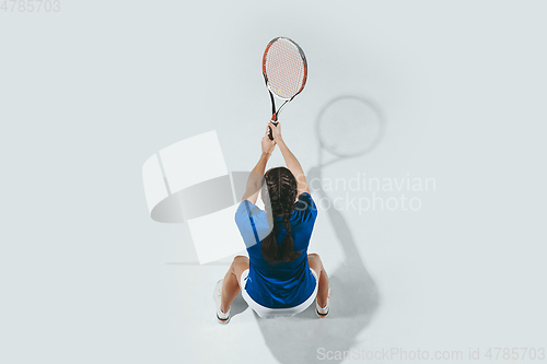 Image of Young woman in blue shirt playing tennis. Youth, flexibility, power and energy.