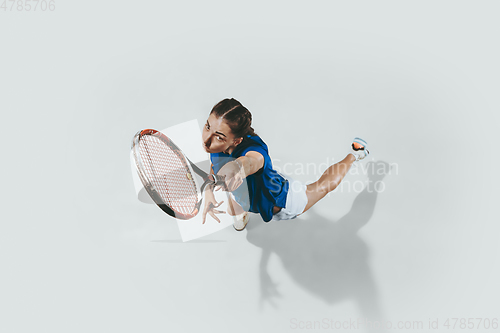 Image of Young woman in blue shirt playing tennis. Youth, flexibility, power and energy.