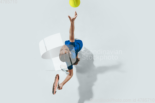 Image of Young woman in blue shirt playing tennis. Youth, flexibility, power and energy.