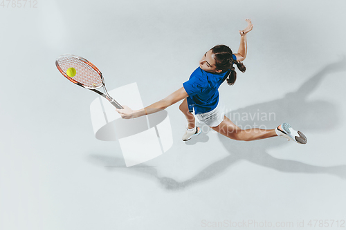 Image of Young woman in blue shirt playing tennis. Youth, flexibility, power and energy.