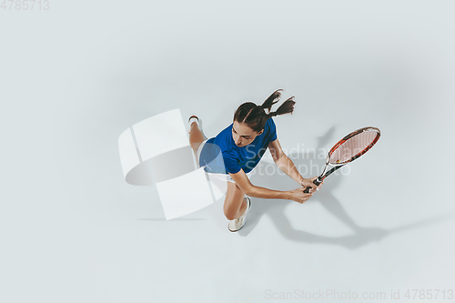 Image of Young woman in blue shirt playing tennis. Youth, flexibility, power and energy.