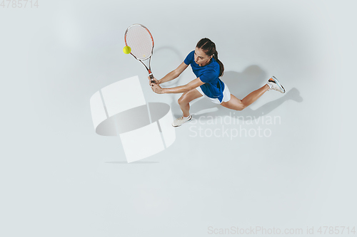 Image of Young woman in blue shirt playing tennis. Youth, flexibility, power and energy.