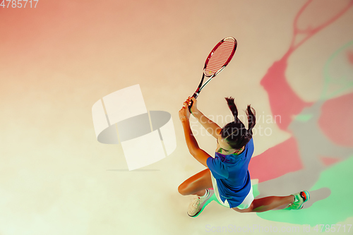 Image of Young woman in blue shirt playing tennis in mixed light. Youth, flexibility, power and energy.