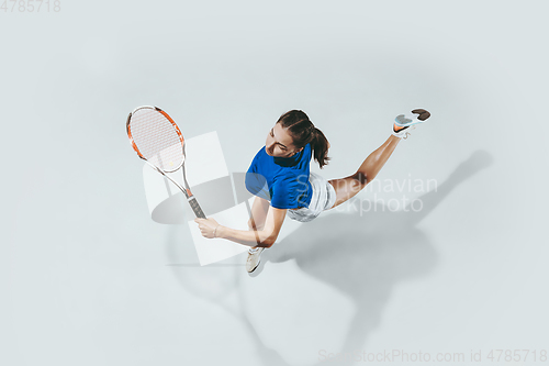 Image of Young woman in blue shirt playing tennis. Youth, flexibility, power and energy.