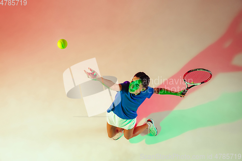 Image of Young woman in blue shirt playing tennis in mixed light. Youth, flexibility, power and energy.