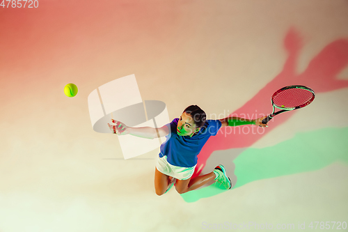 Image of Young woman in blue shirt playing tennis in mixed light. Youth, flexibility, power and energy.