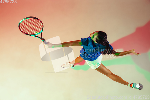 Image of Young woman in blue shirt playing tennis in mixed light. Youth, flexibility, power and energy.