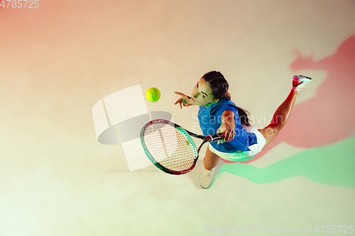 Image of Young woman in blue shirt playing tennis in mixed light. Youth, flexibility, power and energy.