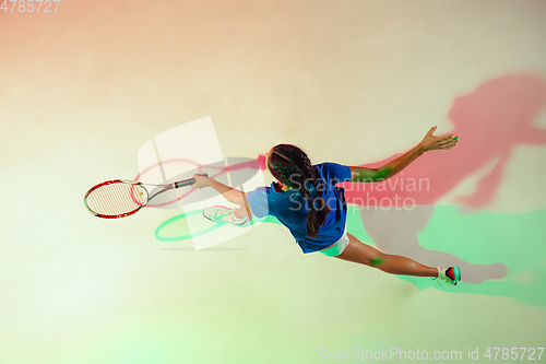 Image of Young woman in blue shirt playing tennis in mixed light. Youth, flexibility, power and energy.