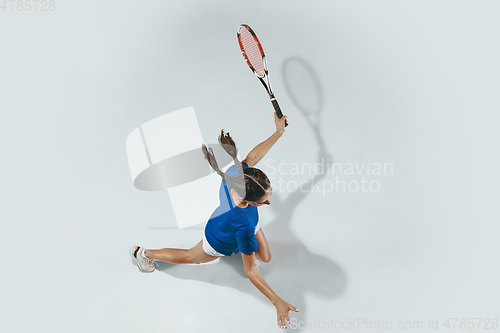 Image of Young woman in blue shirt playing tennis. Youth, flexibility, power and energy.