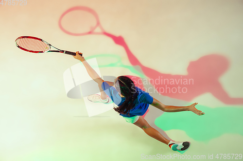 Image of Young woman in blue shirt playing tennis in mixed light. Youth, flexibility, power and energy.