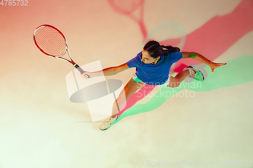 Image of Young woman in blue shirt playing tennis in mixed light. Youth, flexibility, power and energy.