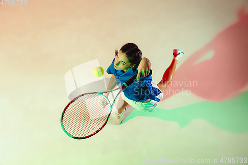 Image of Young woman in blue shirt playing tennis in mixed light. Youth, flexibility, power and energy.