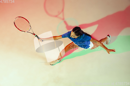 Image of Young woman in blue shirt playing tennis in mixed light. Youth, flexibility, power and energy.