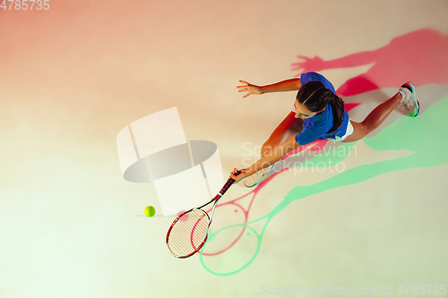 Image of Young woman in blue shirt playing tennis in mixed light. Youth, flexibility, power and energy.