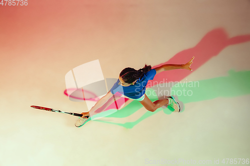 Image of Young woman in blue shirt playing tennis in mixed light. Youth, flexibility, power and energy.