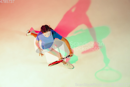 Image of Young woman in blue shirt playing tennis in mixed light. Youth, flexibility, power and energy.