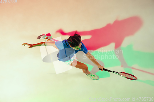 Image of Young woman in blue shirt playing tennis in mixed light. Youth, flexibility, power and energy.