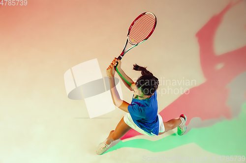 Image of Young woman in blue shirt playing tennis in mixed light. Youth, flexibility, power and energy.