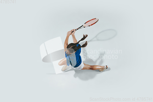 Image of Young woman in blue shirt playing tennis. Youth, flexibility, power and energy.