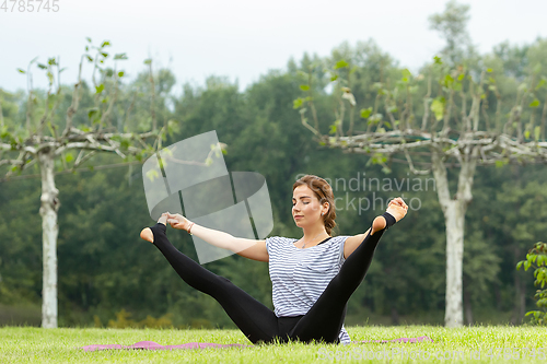 Image of Young beautiful woman doing yoga exercise in green park. Healthy lifestyle and fitness concept.