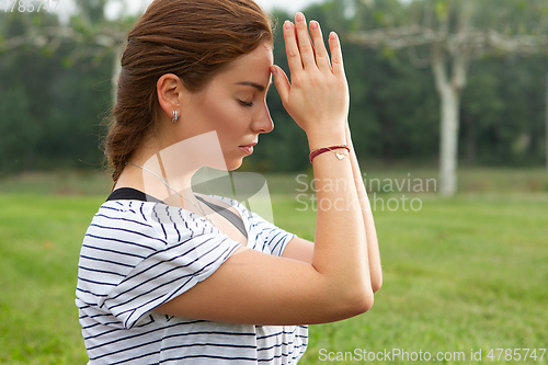 Image of Young beautiful woman doing yoga exercise in green park. Healthy lifestyle and fitness concept.